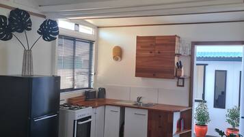 A modern kitchen with a gas stove, oven, and a built-in dishwasher. There is a window with blinds, a wooden cabinet, and a small sink.