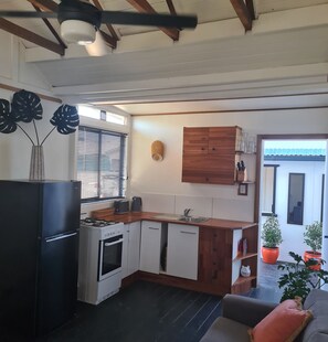 A modern kitchen with a gas stove, oven, and a built-in dishwasher. There is a window with blinds, a wooden cabinet, and a small sink. - Private cottage, dog friendly, close to beach, shops,  bush walks, fishing, more (Ettalong Beach)