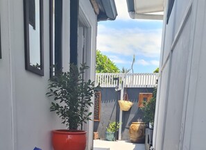 A narrow outdoor corridor with a potted plant, a hanging basket, and a small table. - Private cottage, dog friendly, close to beach, shops,  bush walks, fishing, more (Ettalong Beach)