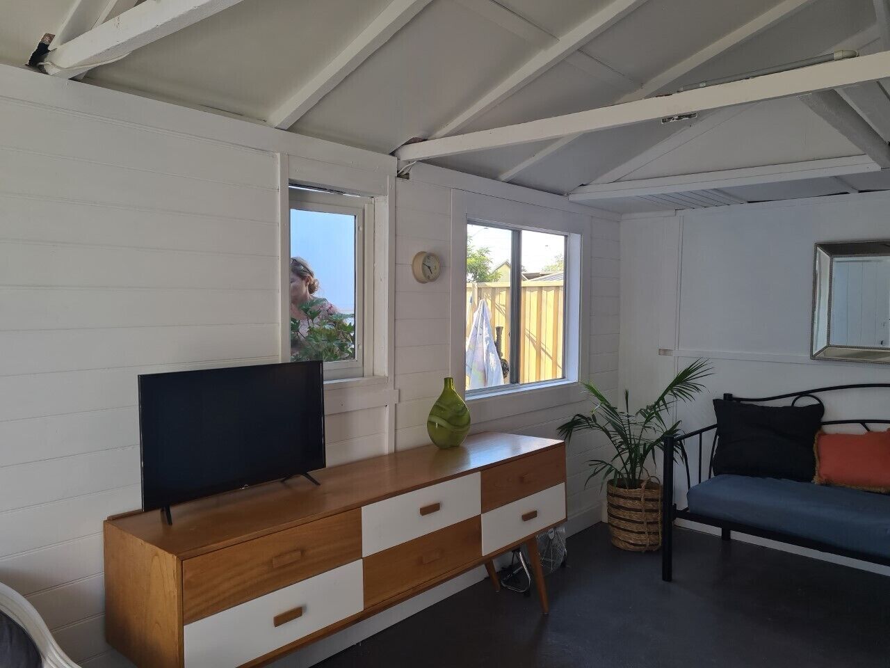 A room with a wooden dresser, a television, a window with a view, a sofa, and a potted plant.