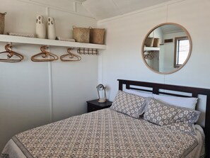A bedroom with a patterned bedspread, a round mirror, and a bedside table with a lamp. - Private cottage, dog friendly, close to beach, shops,  bush walks, fishing, more (Ettalong Beach)