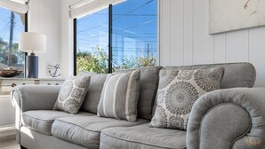 A grey sofa with patterned cushions, a white lamp, and a window with a view of greenery. - Pet Friendly | Remodeled | Private Backyard | FLPCB37 (Panama City Beach)