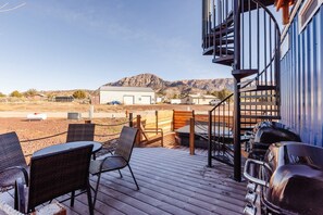En terrasse med udendørs møbler og grill, med udsigt over et ørkenlandskab med bygninger og bjerge.