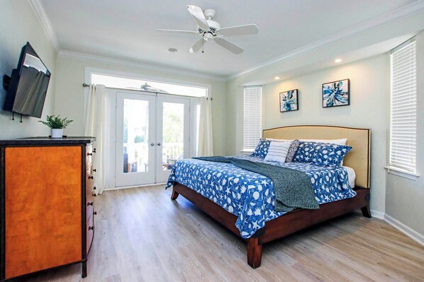 A bedroom with a bed, a dresser, a ceiling fan, and a television.