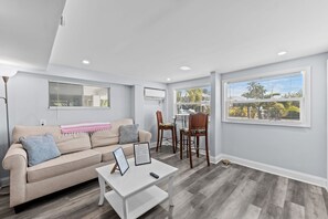 A modern living room with a beige sofa, a white coffee table, and a dining area with two chairs.
