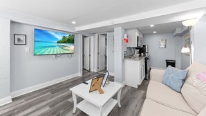 Una sala de estar moderna con un televisor de pantalla plana, una cafetera y un sofá con un cojín decorativo.