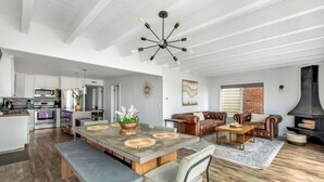 A spacious living area with a dining table, leather sofas, and a fireplace. - Beachfront Sunset Beach, Ocean Views, Sleeps 10 (Huntington Beach)