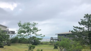 A wooden deck overlooking a grassy area with a 'DOG' sign, a body of water, and buildings in the background. - Beach house Davis Park, Fire Island  (brookhaven)