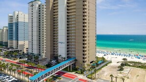 A high-rise hotel with multiple balconies, a beach view, and a pedestrian bridge. - BEACHFRONT Condo! FREE BEACH SERVICE! Sleeps 8! 2Bed 2Bath + Sleeper (Panama City Beach)