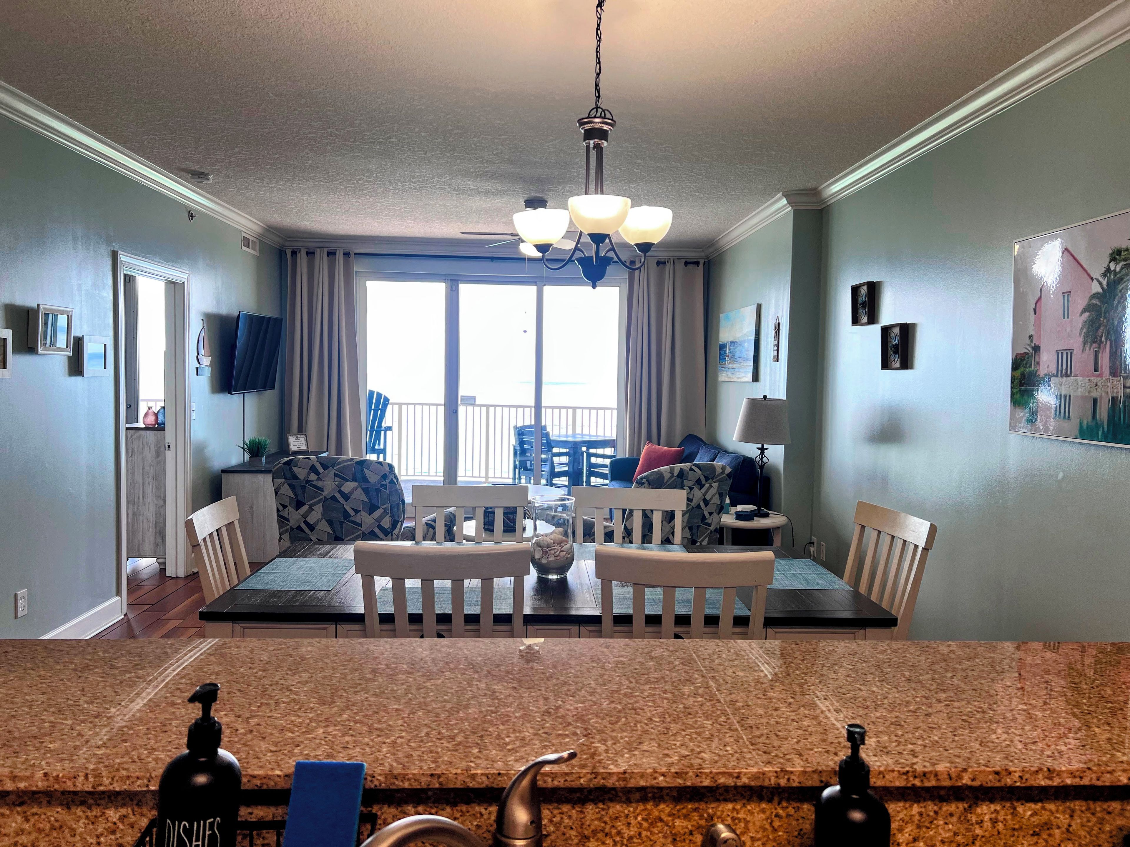 A dining area with a granite countertop, a chandelier, and a view of the outdoors through large windows.