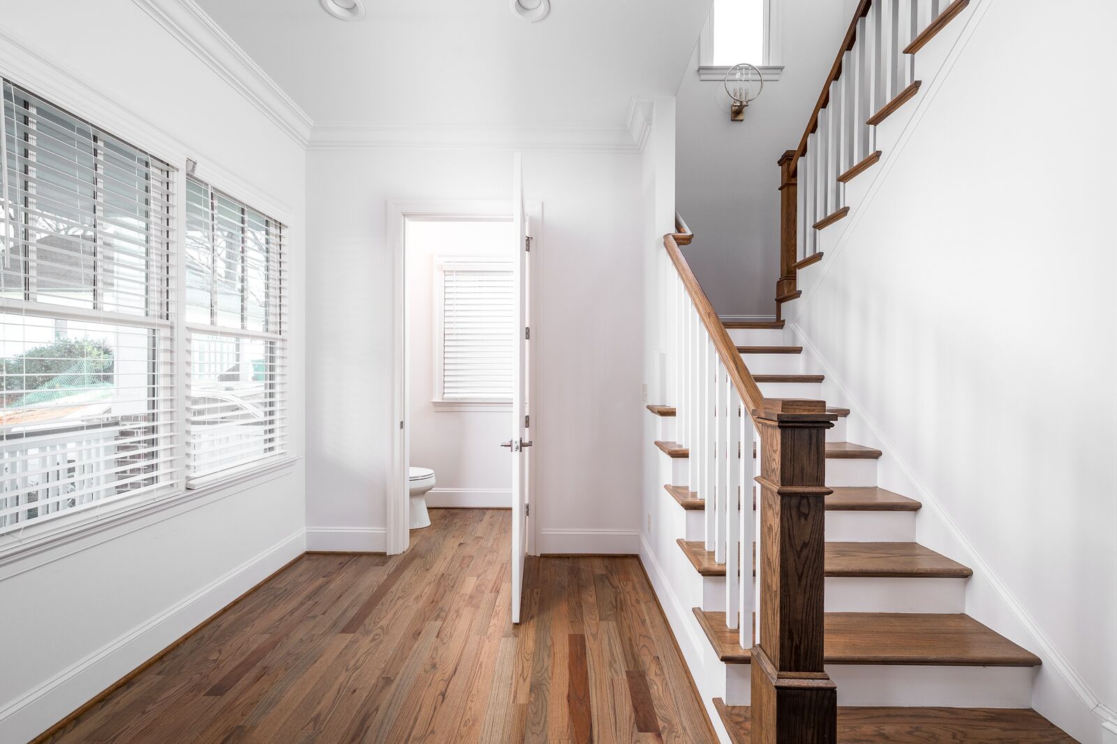 A hallway with wooden flooring, white walls, and a wooden staircase with white railings.