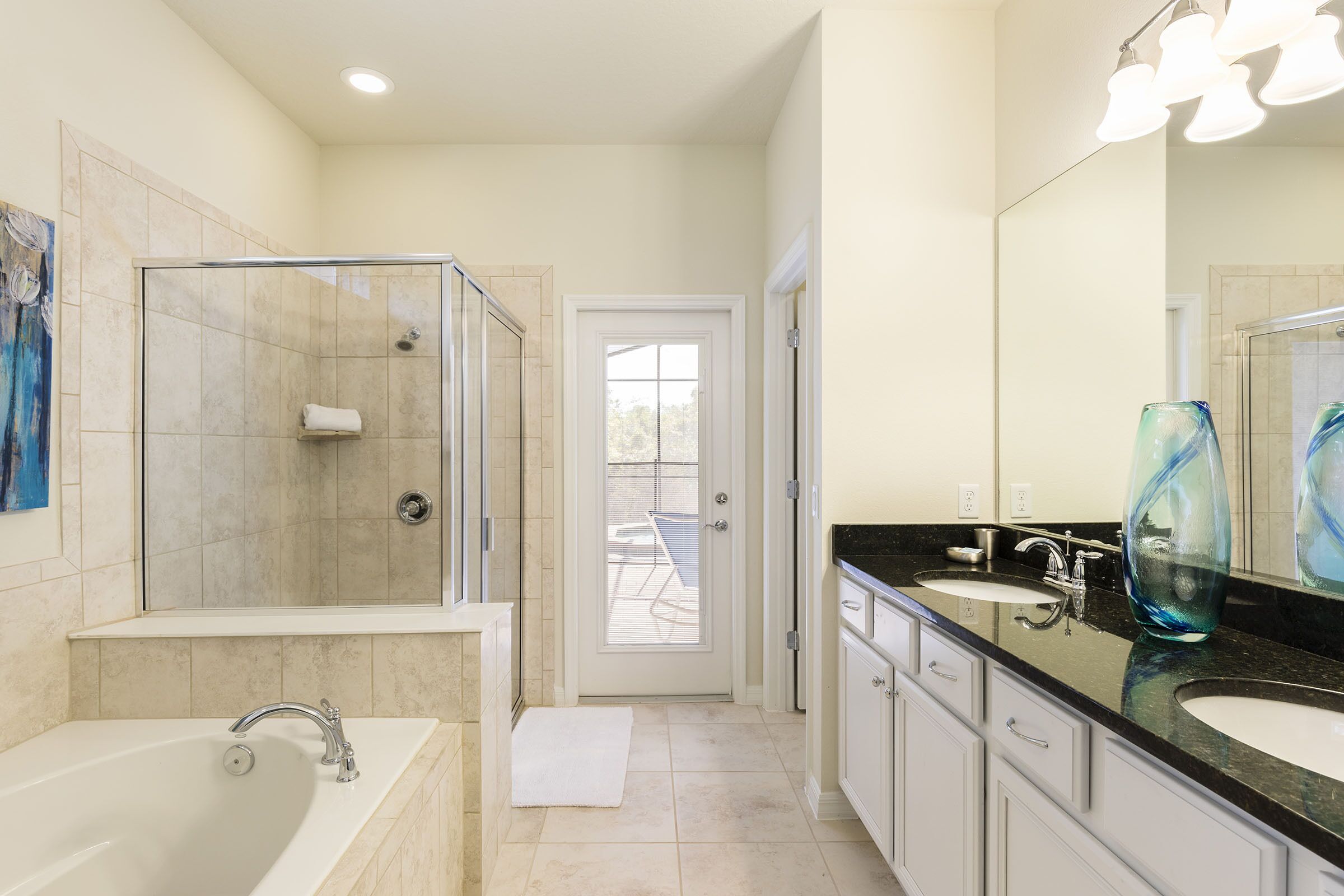 A modern bathroom with a glass-enclosed shower, a large bathtub, and a vanity with two sinks.