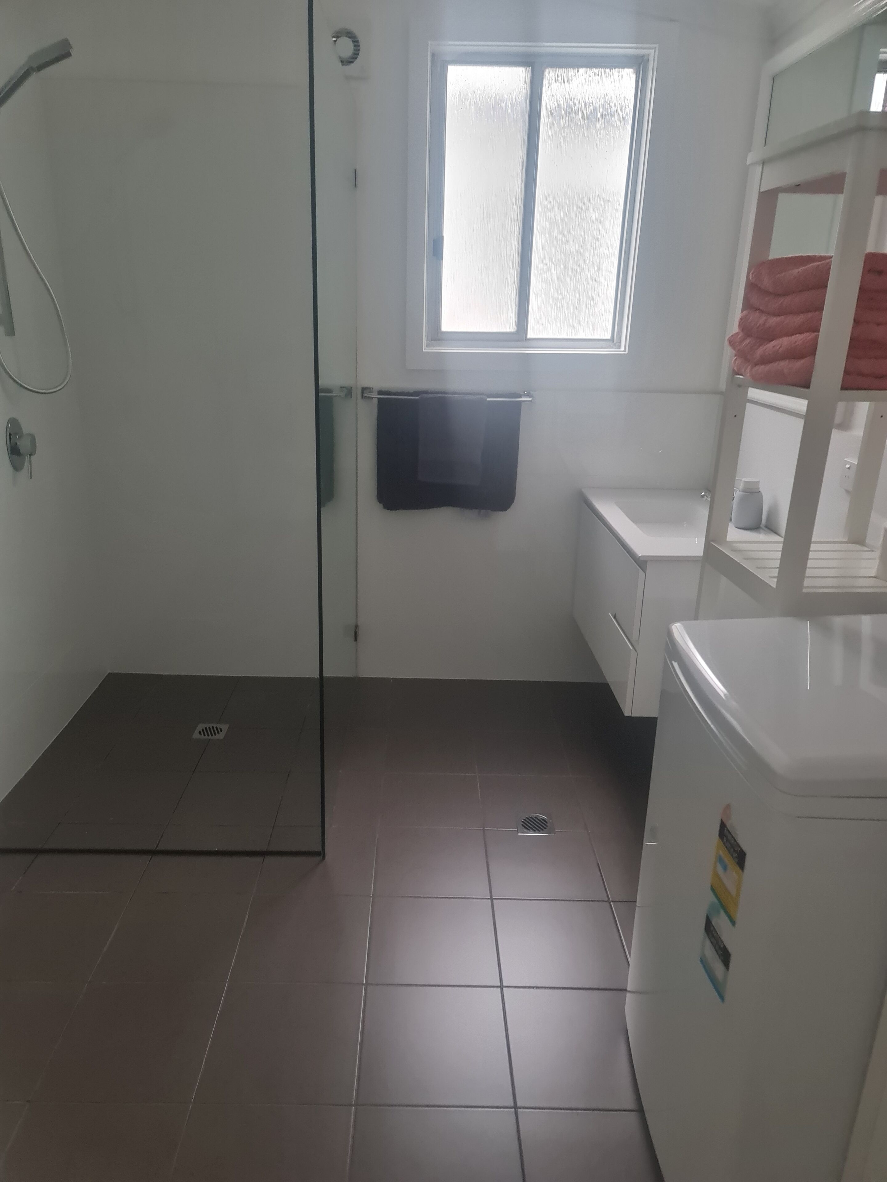 A bathroom with a shower, a window, a towel rack, and a toilet.