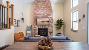 Een woonkamer met een met baksteen beklede open haard, een houten tafel en een bank.