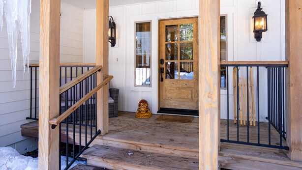 Een houten veranda met een zwarte balustrade, een houten deur en een welkomstmat.