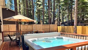 Een hottub omgeven door een houten terras, een tafel met stoelen en een grote parasol.