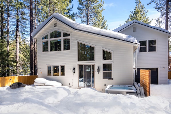 A two-story house with a snow-covered roof and a hot tub in the front yard.