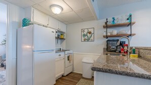A compact kitchen with white appliances, a wooden floor, and a small trash bin.