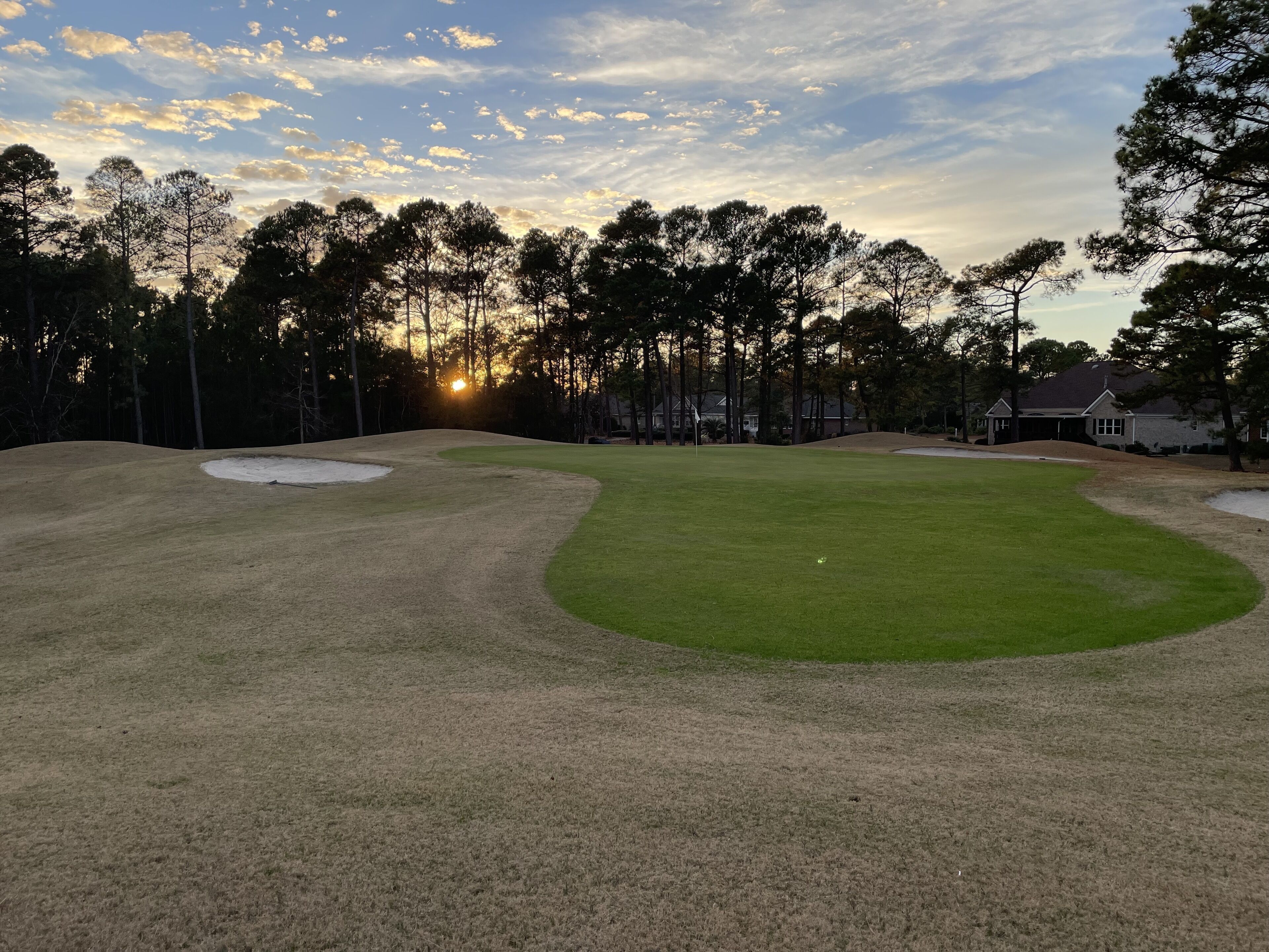 Un campo de golf con búnkeres de arena, un putting green y un club de campo al fondo.