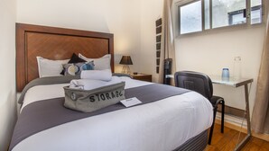 A hotel room with a bed, a desk, a chair, a nightstand, and a window with curtains. - Essential Room in Condesa + Rooftop & Coworking - Omega by Nomadier (Ciudad de México)