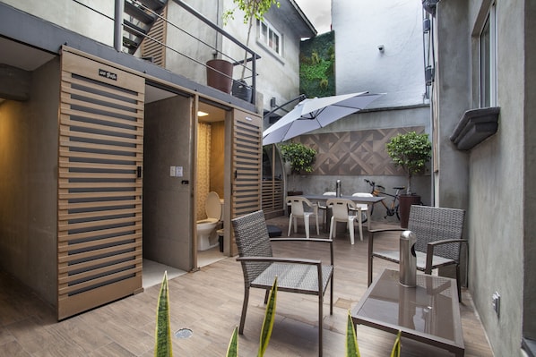 Un patio moderno al aire libre con una mesa de comedor, sillas y una sombrilla grande.