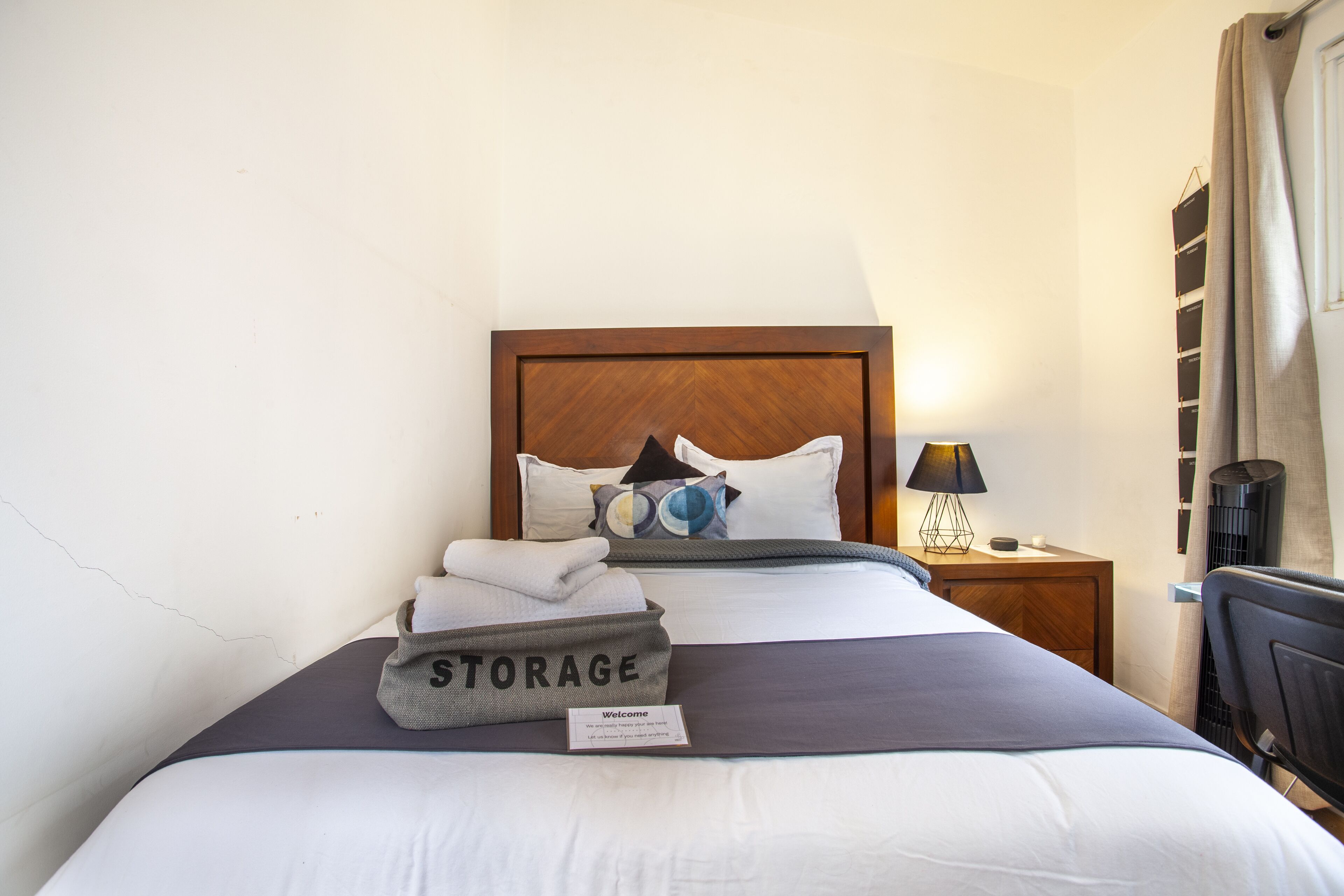 A neatly made bed with a storage bin labeled 'STORAGE' and a welcome card.