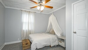Un dormitorio con cama, ventilador de techo, mesita de noche, armario y ventana con cortinas.