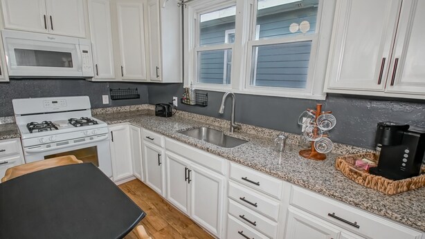 Una cocina moderna con armarios blancos, encimera de granito, estufa, fregadero y ventana con persianas.