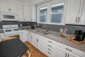 Una cocina moderna con armarios blancos, encimera de granito, estufa, fregadero y ventana con persianas.