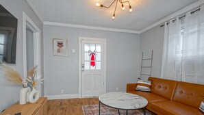 Una sala de estar con una mesa redonda, un sofá, una puerta decorada con un adorno rojo y una araña.