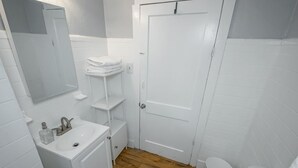 Un baño con elementos blancos, suelo de madera, inodoro blanco y cubo de basura de mármol.