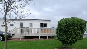 Una casa móvil con terraza, un arbolillo y un patio cubierto de césped.
