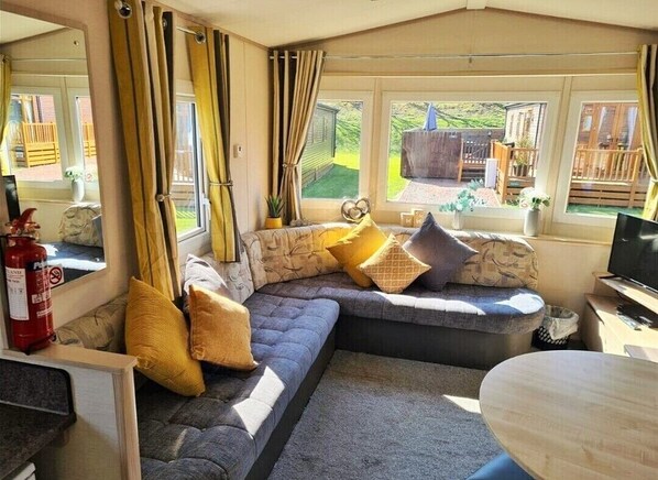 Relax in a comfortable seating area with a sofa and small table, surrounded by serene views of a wooden deck and lush greenery.