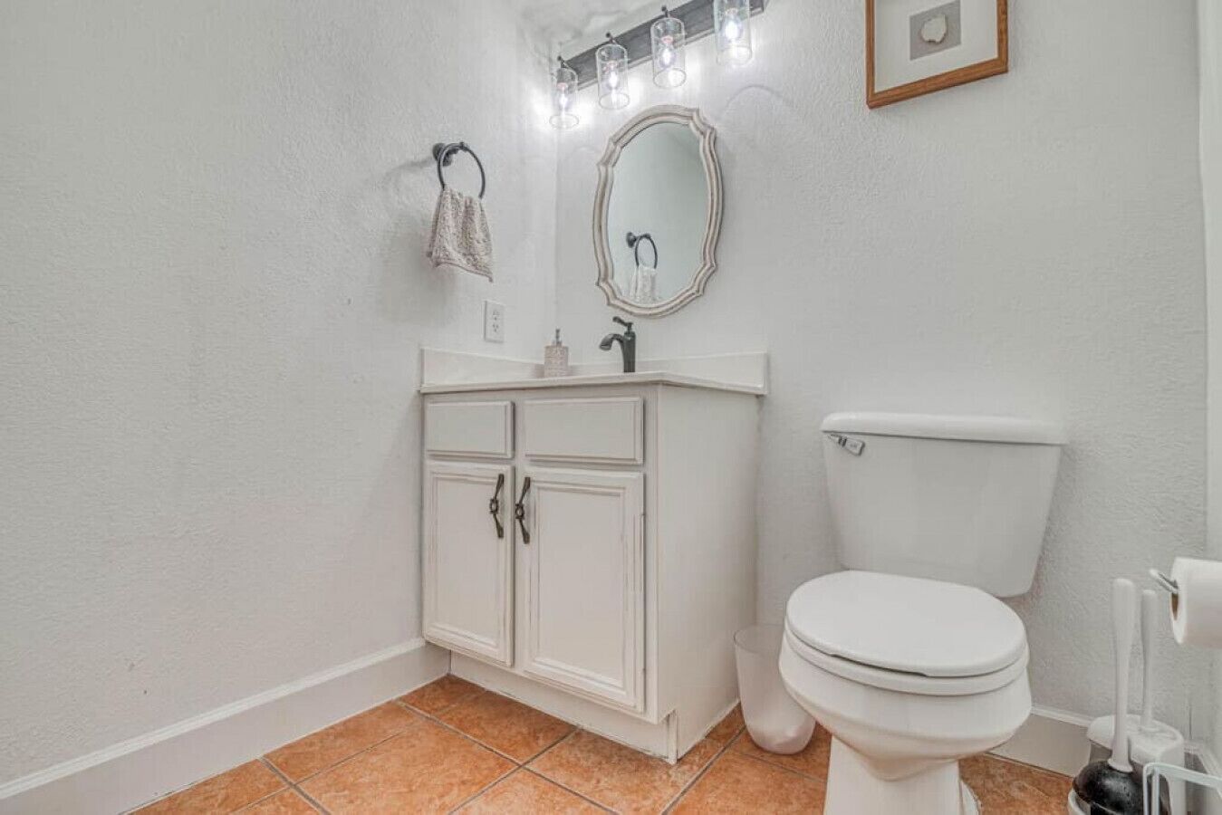 Une salle de bain avec des toilettes blanches, un meuble avec deux portes, un miroir et une serviette accrochée au mur.