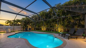 Une piscine extérieure dotée d’une structure en verre, entourée de palmiers et agrémentée d’un barbecue.
