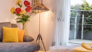 A room with a sofa, a lamp, a vase with flowers, and a view of greenery outside. - Studio Apartment 'B + E Röck' with Private Balcony and Wi-Fi (Meckenbeuren)