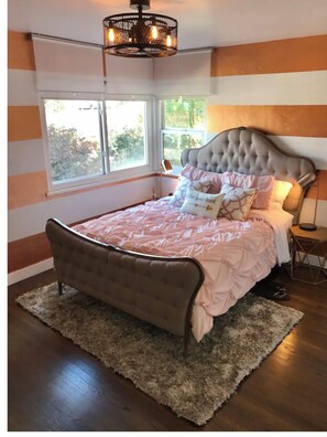 A bedroom with a tufted headboard, a large window, and a chandelier.