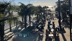 Un área de estar al aire libre con mesas y sillas, palmeras y vista a la playa.