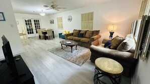 Una sala de estar con sofá, una mesa de centro y un mueble para televisión. Hay un comedor con una mesa y sillas.