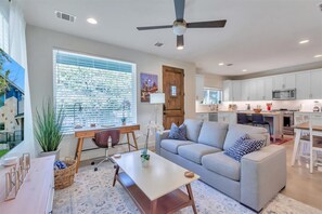 A modern living room with a grey sofa, a wooden coffee table, and a dining area with a white table and chairs.