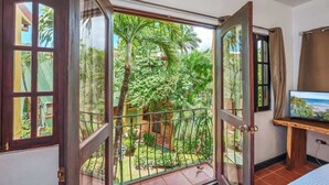A room with a large sliding glass door leading to a lush garden with palm trees and a view of a beach. - Quiet Tamarindo 2BR | 10-min Walk to the Beach! (Tamarindo)