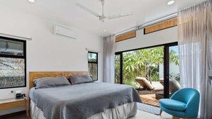 Ein modernes Schlafzimmer mit einem großen Bett, einem Deckenventilator und Blick ins Freie durch eine Schiebetür.