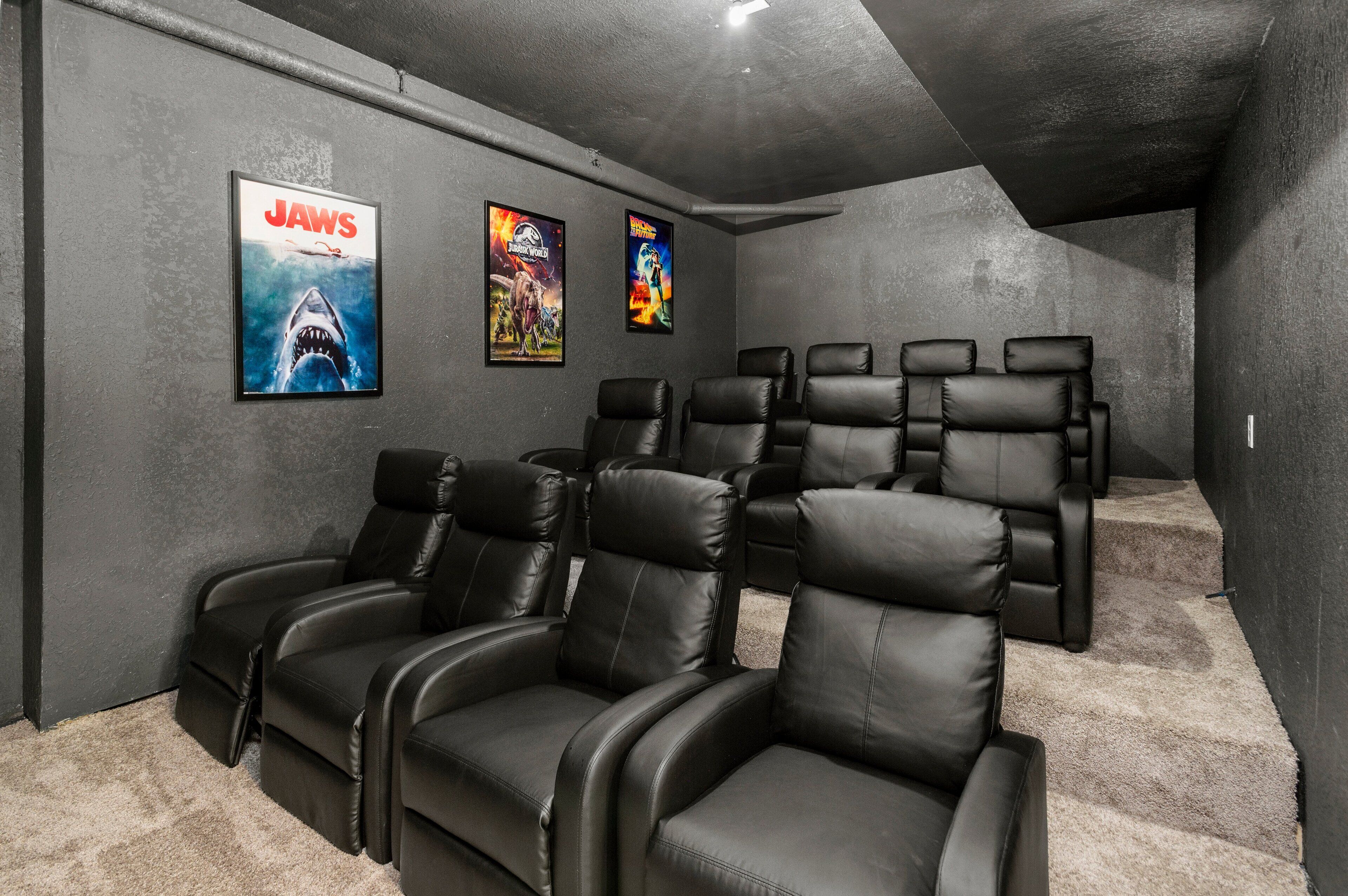A home theater room with black leather reclining chairs and three movie posters on the wall.