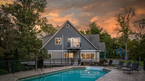 Ein zweistöckiges Haus mit Swimmingpool, umzäunter Terrasse und Gartenmöbeln.