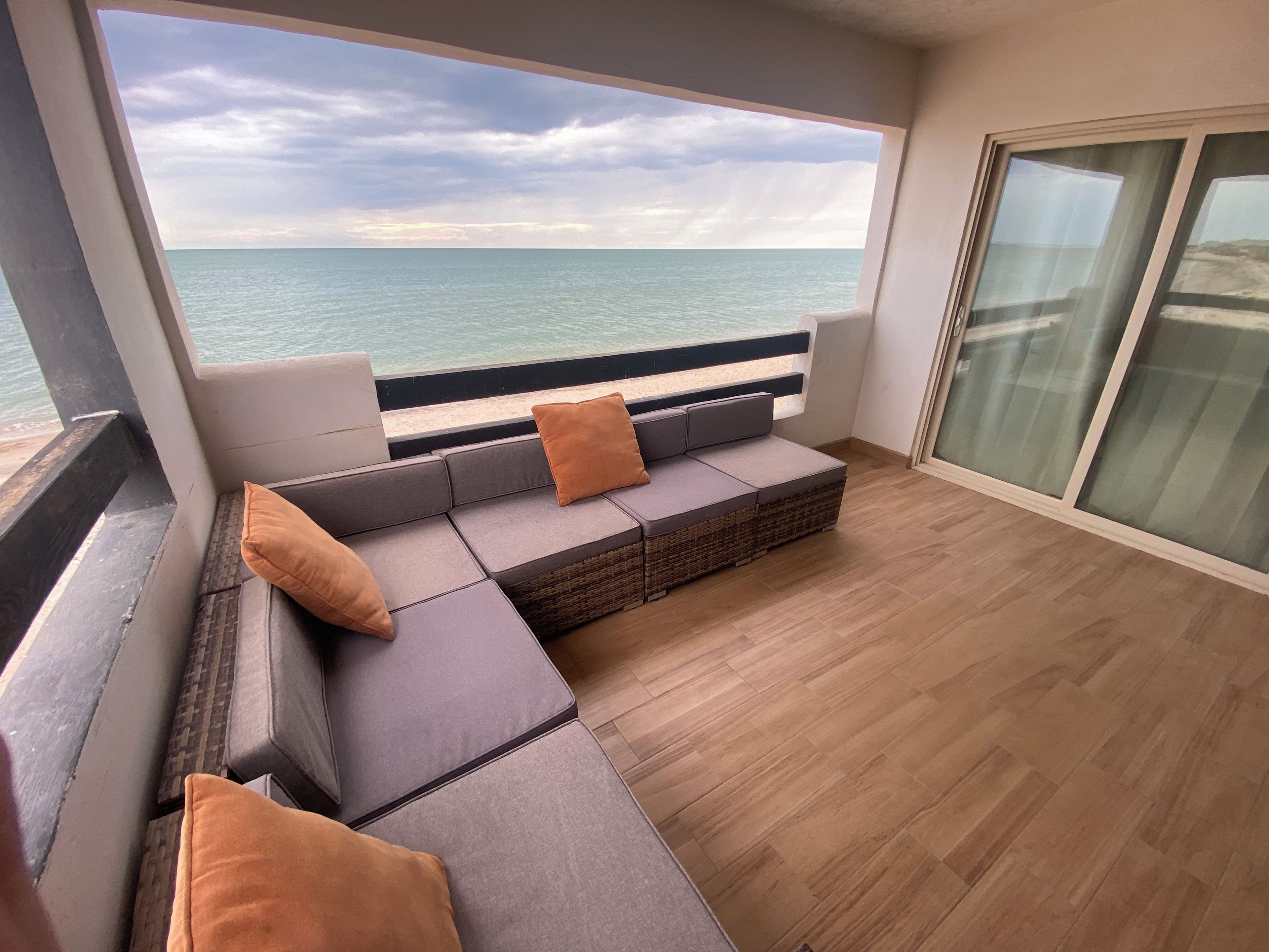 Un balcon avec un canapé et des coussins, une vue sur la mer et un plancher en bois.
