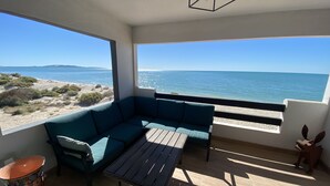 Ein Zimmer mit großem Fenster zum Strand, ein blaues Sofa und ein Holztisch.