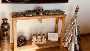 Ein Wohnzimmer mit einem großen Flachbildfernseher an der Wand, einem Holzkonsolentisch mit Dekoration, einem Metall-Weihnachtsbaum und einer kleinen Buddha-Statue.