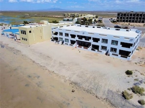 A multi-story hotel with a flat roof, a swimming pool, and a desert landscape in the background.