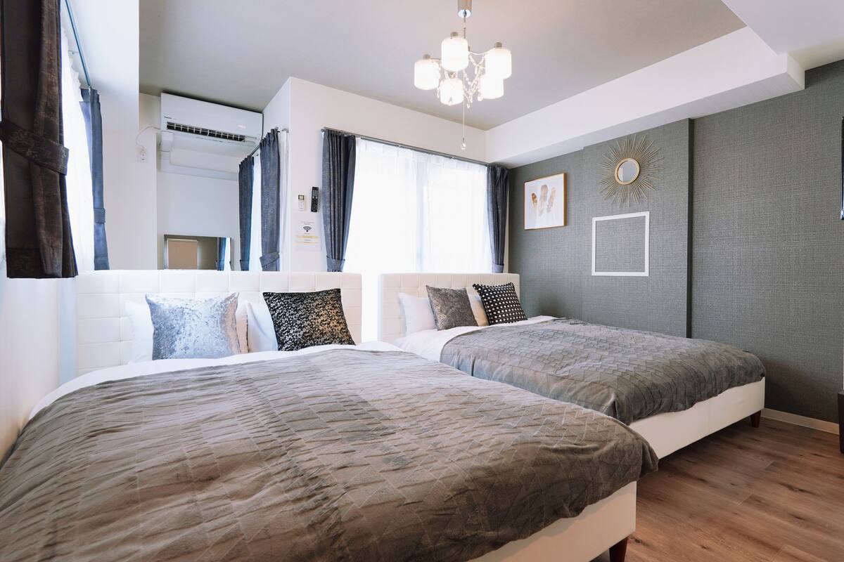 Un dormitorio moderno con dos camas, una araña, un ventanal con cortinas y un televisor de pared.