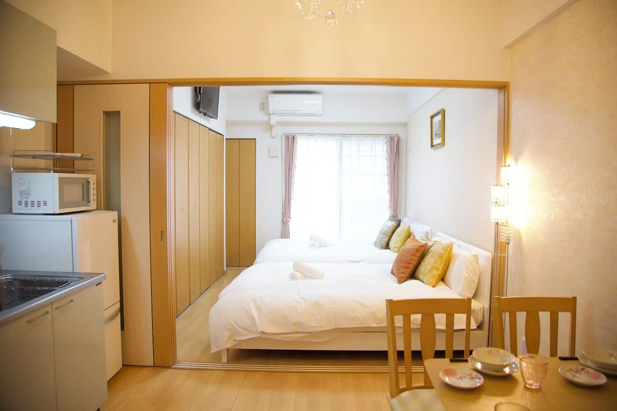 Una habitación de hotel compacta con cama, mesita de noche y una pequeña cocina equipada con microondas.